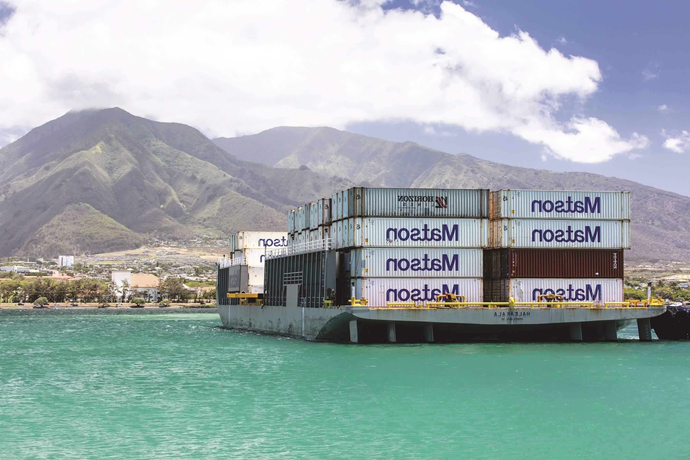 满载澳博体育app下载集装箱的澳博体育app下载驳船Haleakala抵达Kahului，背景是绿色的山脉和云彩.
